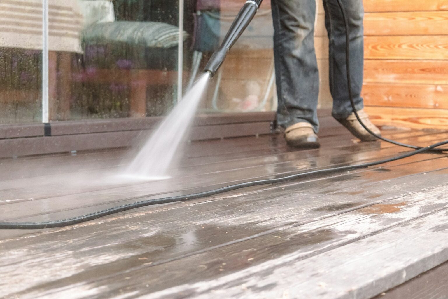 Man cleaning walls and floor with high pressure power washer. Washing terrace wood planks and claddi