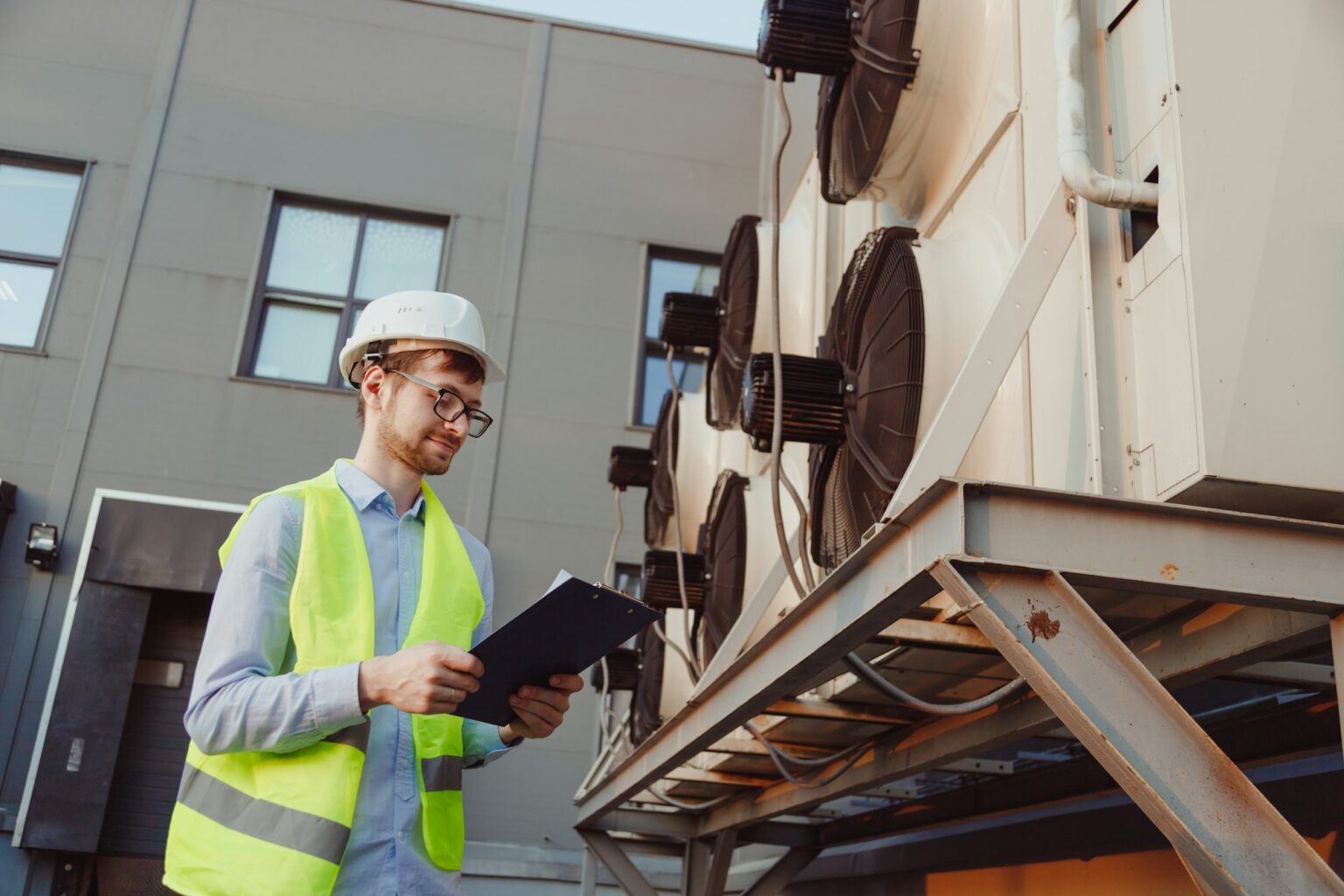 Service engineer in uniform inspecting industrial refrigeration system, outdoor refrigeration plant